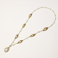 Long gold-plated necklace with eye-shaped elements, freshwater pearls, and baroque pearl pendant on neutral background.