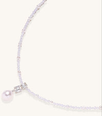 Delicate beaded necklace with lavender crystals, white pearls, and crystal pendant with pearl drop on white background.