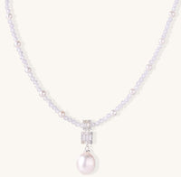 Delicate beaded necklace with lavender crystals, white pearls, and crystal pendant with pearl drop on white background.