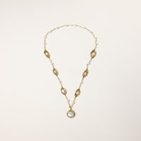Long gold-plated necklace with eye-shaped elements, freshwater pearls, and baroque pearl pendant on neutral background.