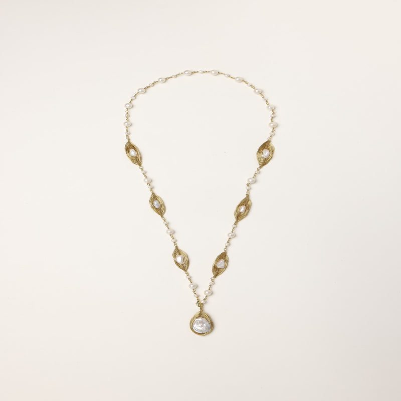 Long gold-plated necklace with eye-shaped elements, freshwater pearls, and baroque pearl pendant on neutral background.