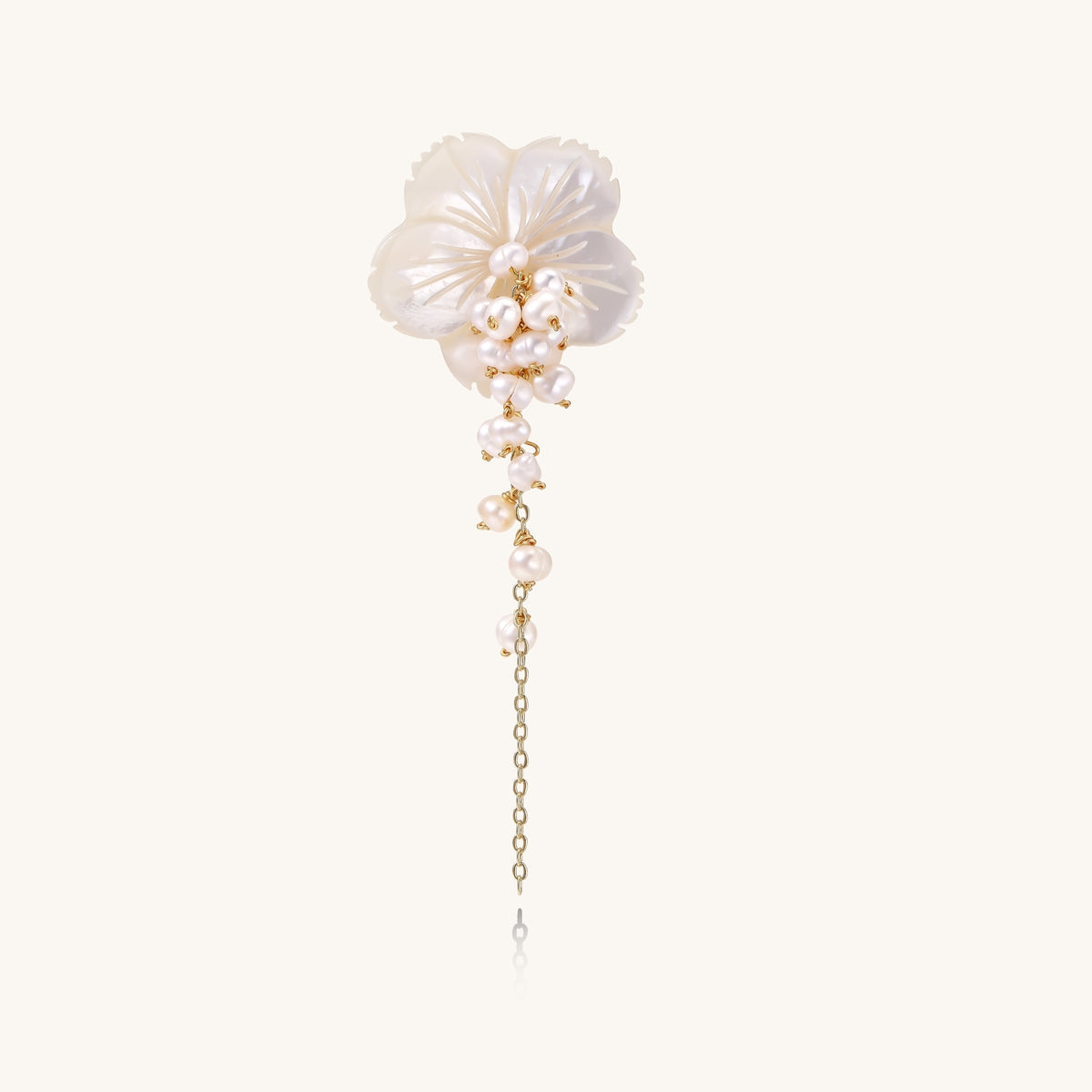 Delicate hair pin featuring translucent shell flower with cascading freshwater pearls on gold chain against cream background.