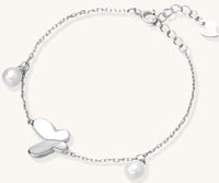 Dainty sterling silver chain bracelet with heart charm and freshwater pearl dangles on white background.