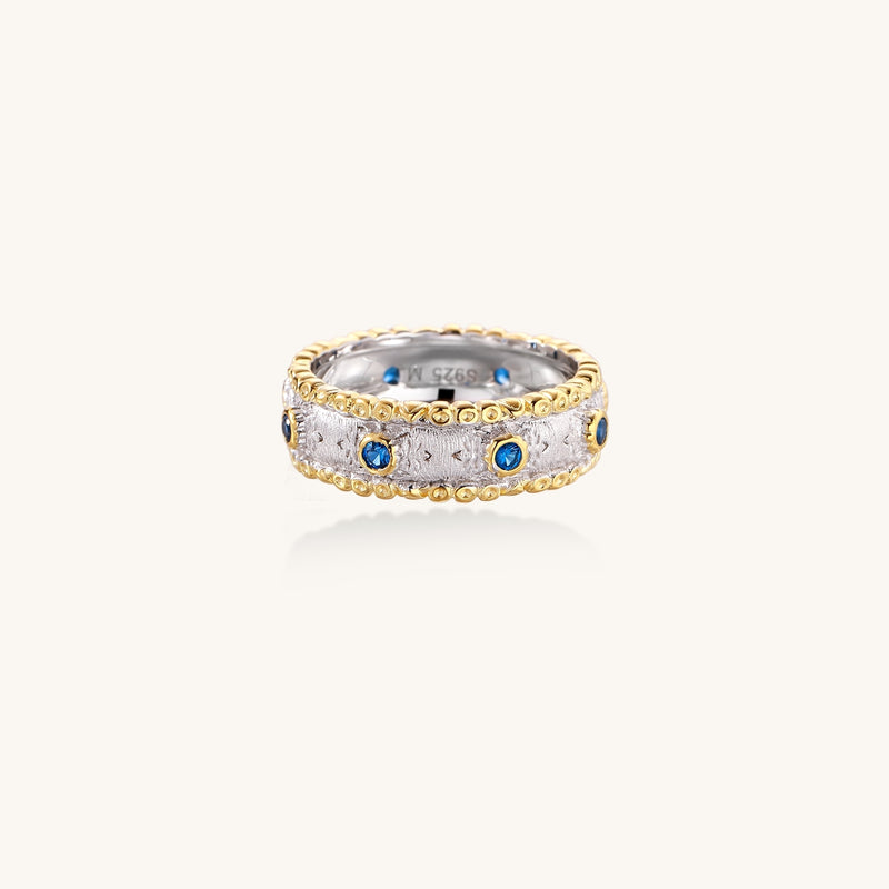 Sterling silver ring with brushed center band, blue zirconia stones, and 24k gold-plated decorative borders.