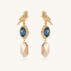 Gold-plated bird dangle earrings with iridescent abalone shell discs and champagne crystal drops on white background.