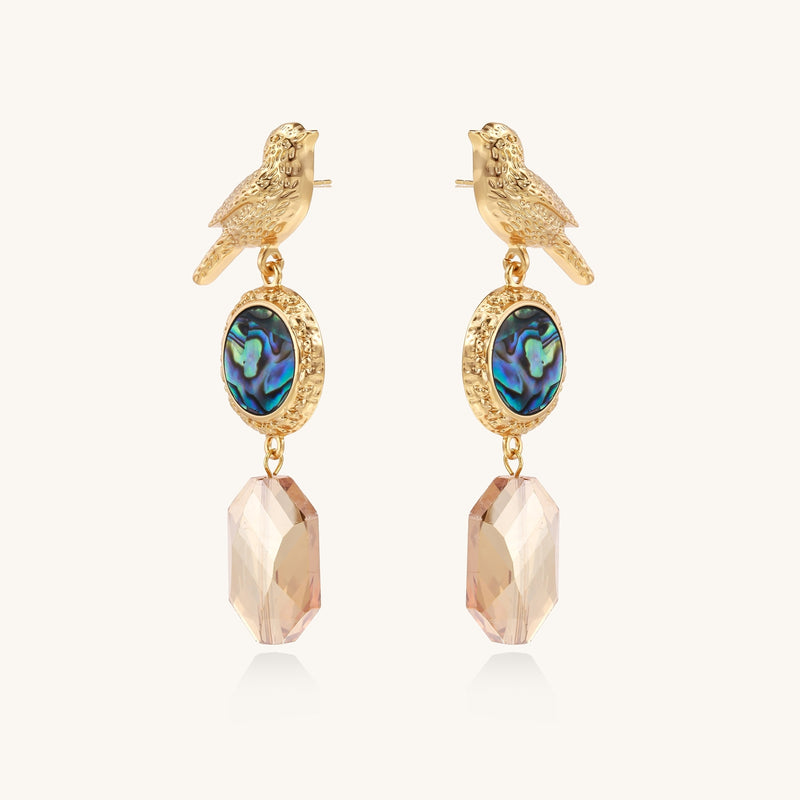 Gold-plated bird dangle earrings with iridescent abalone shell discs and champagne crystal drops on white background.