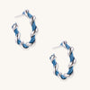 Twisted hoop earrings featuring blue denim fabric braided with gold-plated metal in a spiral design on white background.
