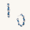 Twisted hoop earrings featuring blue denim fabric braided with gold-plated metal in a spiral design on white background.