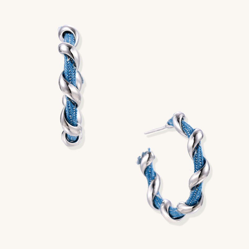 Twisted hoop earrings featuring blue denim fabric braided with gold-plated metal in a spiral design on white background.