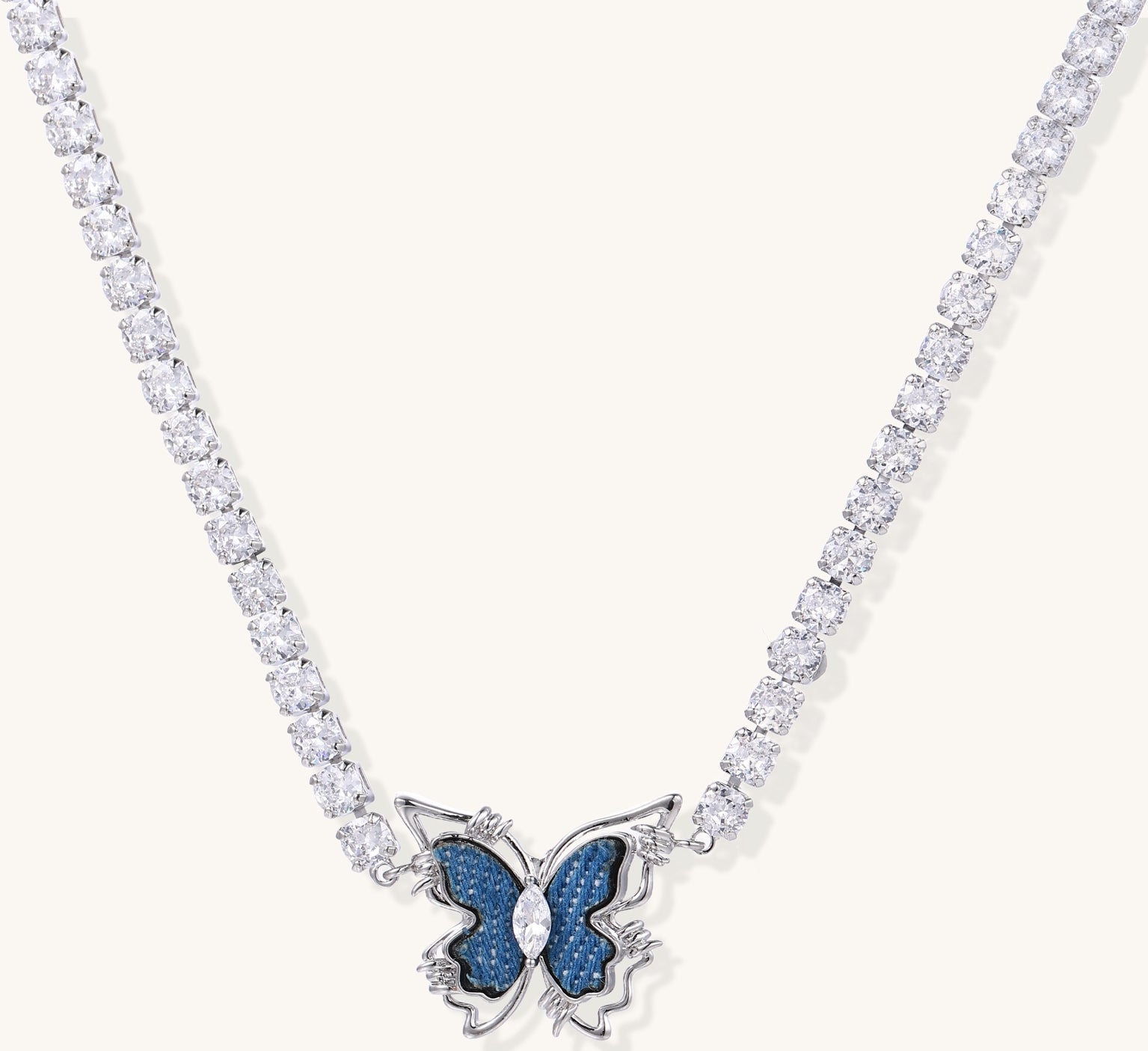 Gold-plated tennis chain necklace with blue denim butterfly pendant and zirconia stones on light background.