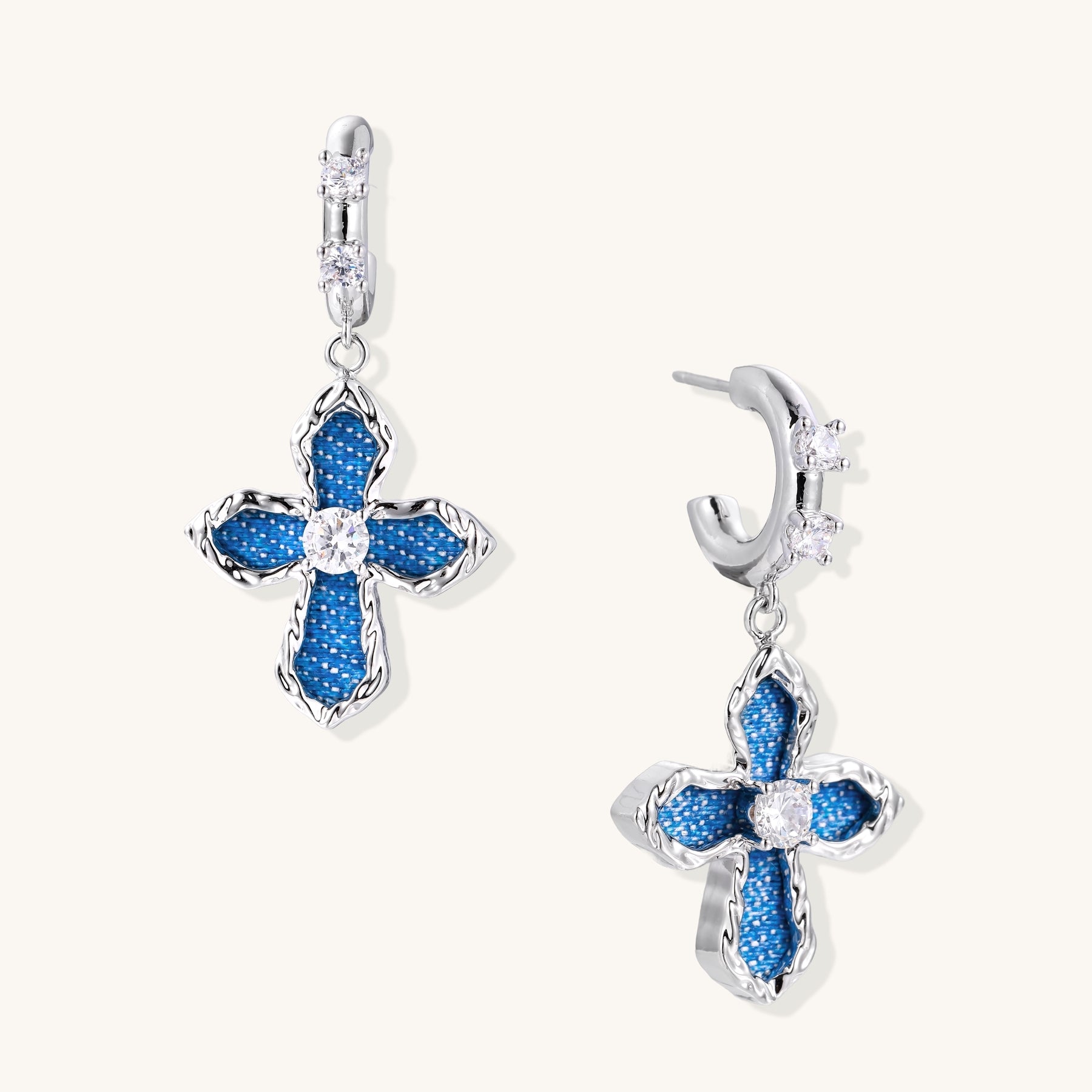 Gold-plated huggie earrings with blue denim-textured cross charms and clear zirconia center stones on white background.