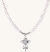 Elegant pearl necklace with ornate 18K gold plated cross pendant featuring zirconia stones on neutral background.