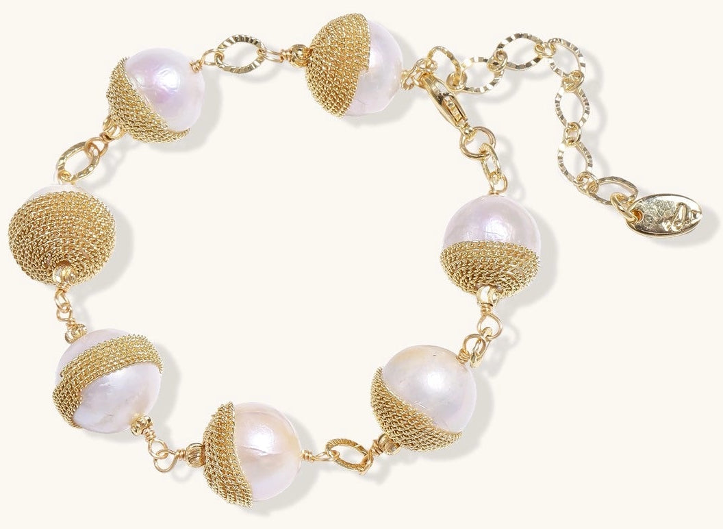 Adjustable bracelet featuring baroque pearls wrapped in gold mesh wire with delicate chain links on cream background.