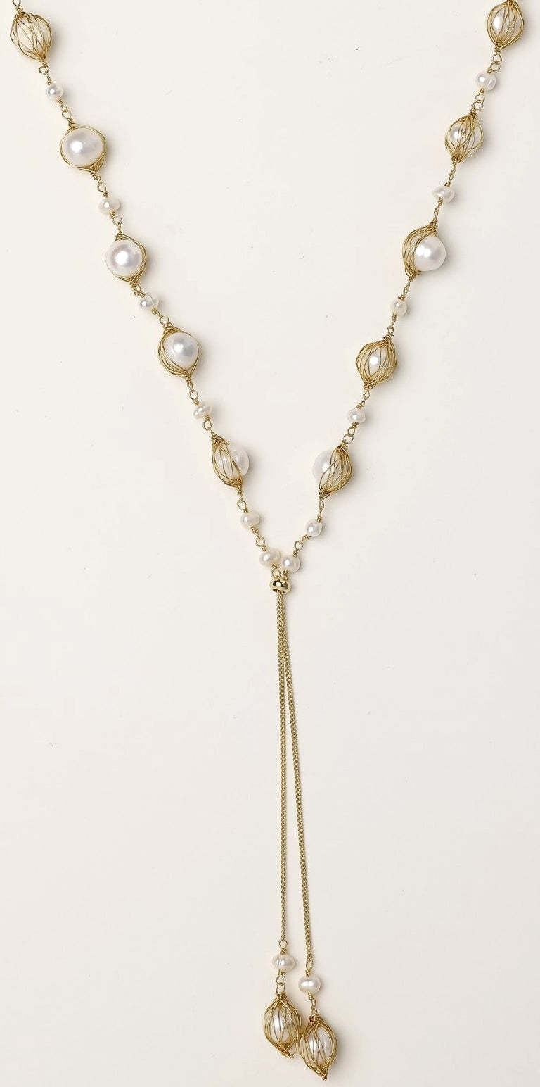 Long gold-plated lariat necklace with wire-wrapped freshwater pearls and chain tassel detail on cream background.