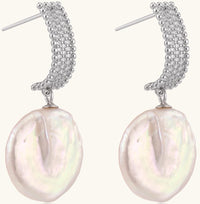 Sterling silver huggie earrings with lustrous baroque pearls displaying iridescent pink and cream tones on white background.