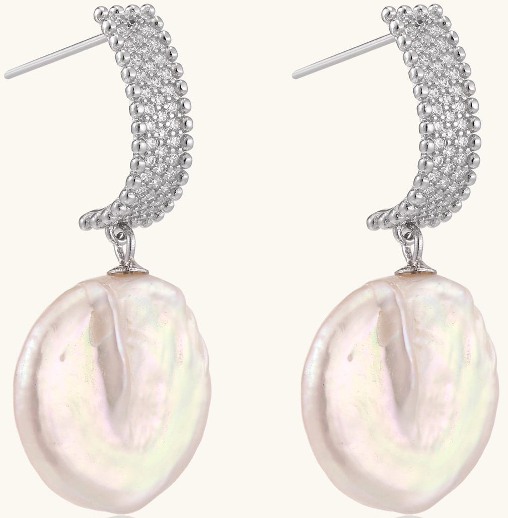 Sterling silver huggie earrings with lustrous baroque pearls displaying iridescent pink and cream tones on white background.