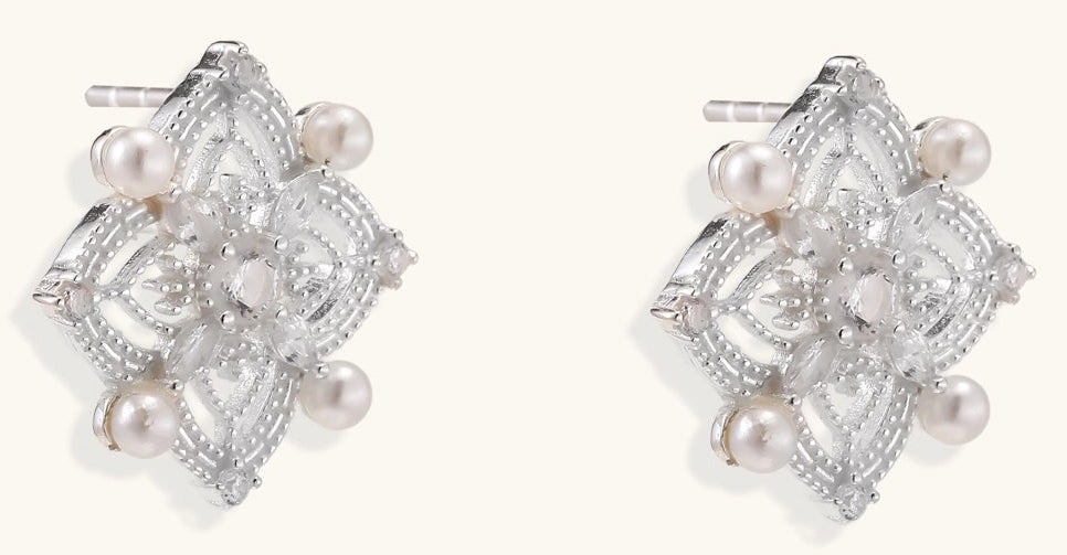 Detailed view of sterling silver stud earrings with geometric filigree design and small freshwater pearls on white background.