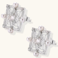 Detailed view of sterling silver stud earrings with geometric filigree design and small freshwater pearls on white background.