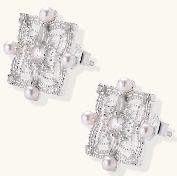 Detailed view of sterling silver stud earrings with geometric filigree design and small freshwater pearls on white background.
