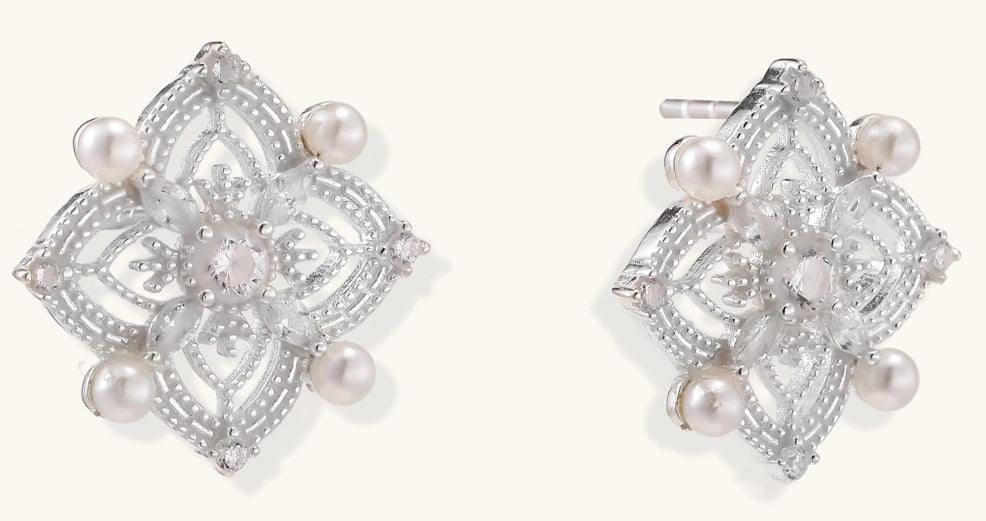 Detailed view of sterling silver stud earrings with geometric filigree design and small freshwater pearls on white background.