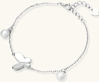 Delicate rhodium-plated silver chain bracelet with butterfly charm and two freshwater pearls on cream background