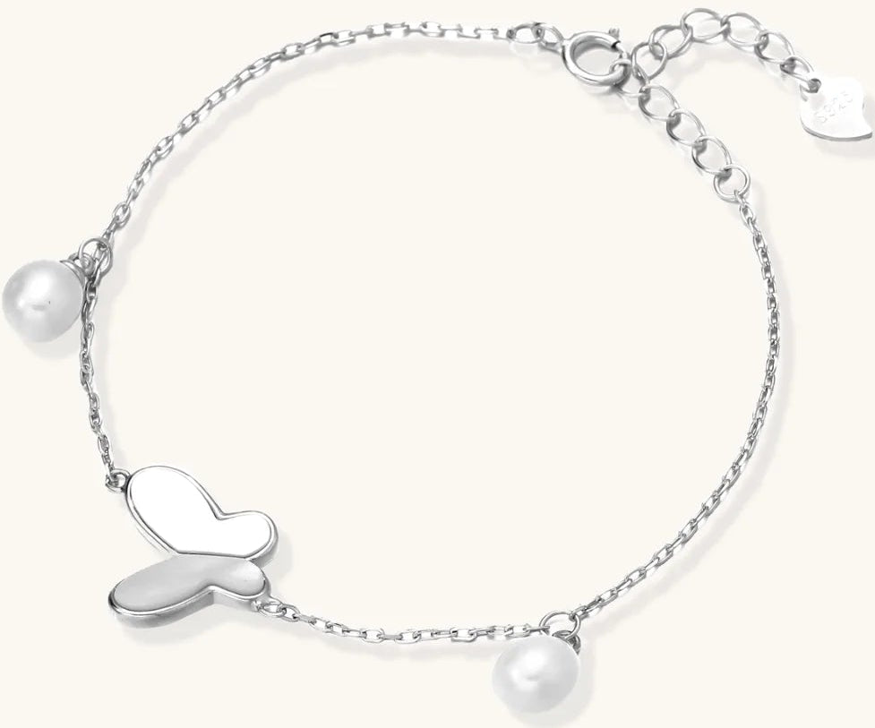 Delicate rhodium-plated silver chain bracelet with butterfly charm and two freshwater pearls on cream background
