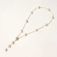 Gold-plated lariat necklace with baroque pearls and textured caps on cream background, showing adjustable Y-shaped design.