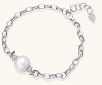 Rhodium-plated silver chain bracelet with single white freshwater pearl and heart charm clasp on cream background