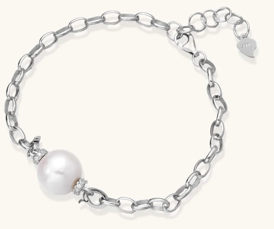 Rhodium-plated silver chain bracelet with single white freshwater pearl and heart charm clasp on cream background