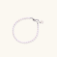 Delicate freshwater pearl bracelet with rhodium-plated silver clasp and single pearl drop charm on cream background