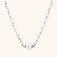 Dainty rhodium-plated silver chain necklace with centered 10mm freshwater pearl and crystal accents on cream background
