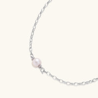 Dainty rhodium-plated silver chain necklace with centered 10mm freshwater pearl and crystal accents on cream background