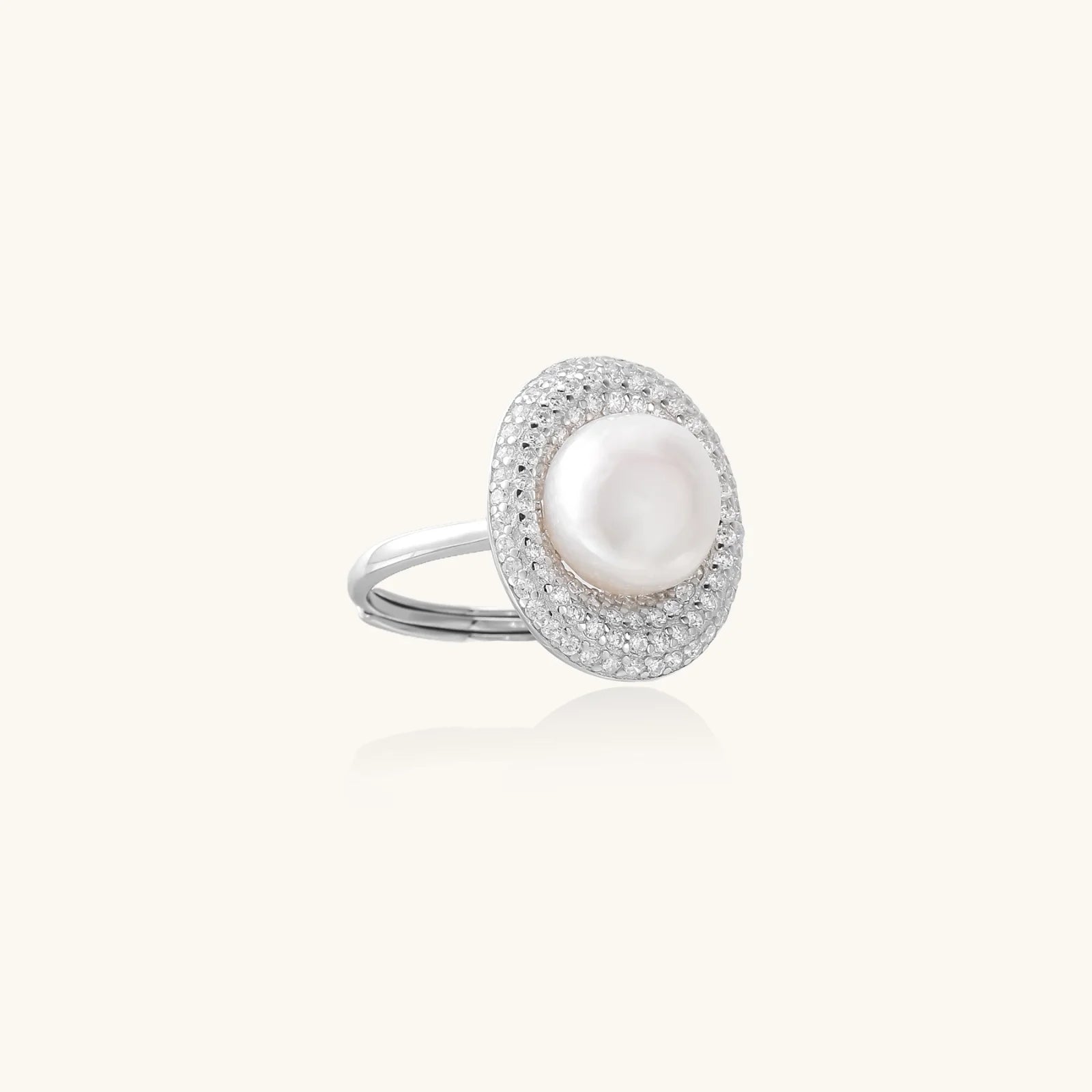 Silver ring with lustrous white pearl center surrounded by sparkling crystal halo on light background.