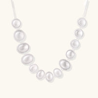 Graduated pearl-finish silver discs forming an organic bubble bib necklace on delicate chain against cream background.