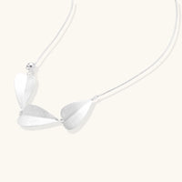 Minimalist sterling silver necklace with three brushed leaf-shaped pendants on delicate chain against white background
