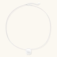 Minimalist brushed sterling silver dome pendant on delicate chain against cream background, showing matte textured finish