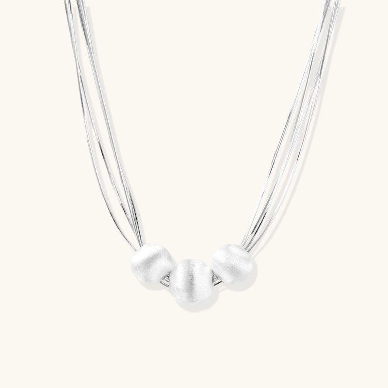 Sterling silver multi-strand necklace with three brushed round beads on cream background
