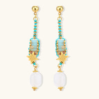 Gold-plated dangle earrings with turquoise threading, star charms, and white pearl beads against cream background.