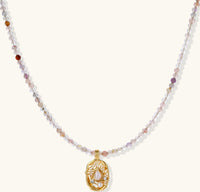 Delicate gold-plated necklace with mixed gemstone beads and ornate oval pendant on white background