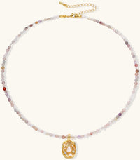 Delicate gold-plated necklace with mixed gemstone beads and ornate oval pendant on white background