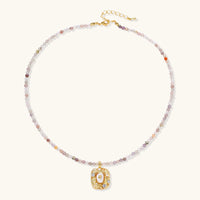Ornate gold-plated pendant necklace with multicolored gemstone beads in purple, pink and clear tones on white background