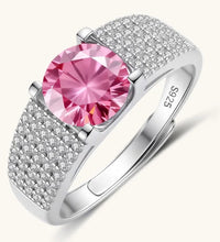 Adjustable sterling silver ring with round pink moissanite center stone and pavé crystal detailing on cream background.