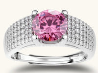 Adjustable sterling silver ring with round pink moissanite center stone and pavé crystal detailing on cream background.