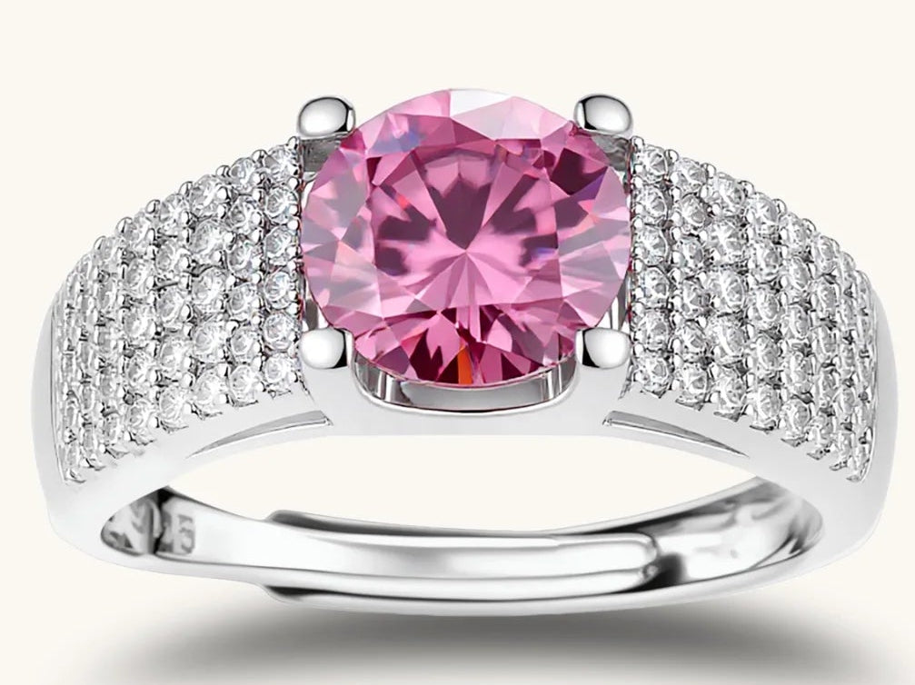 Adjustable sterling silver ring with round pink moissanite center stone and pavé crystal detailing on cream background.