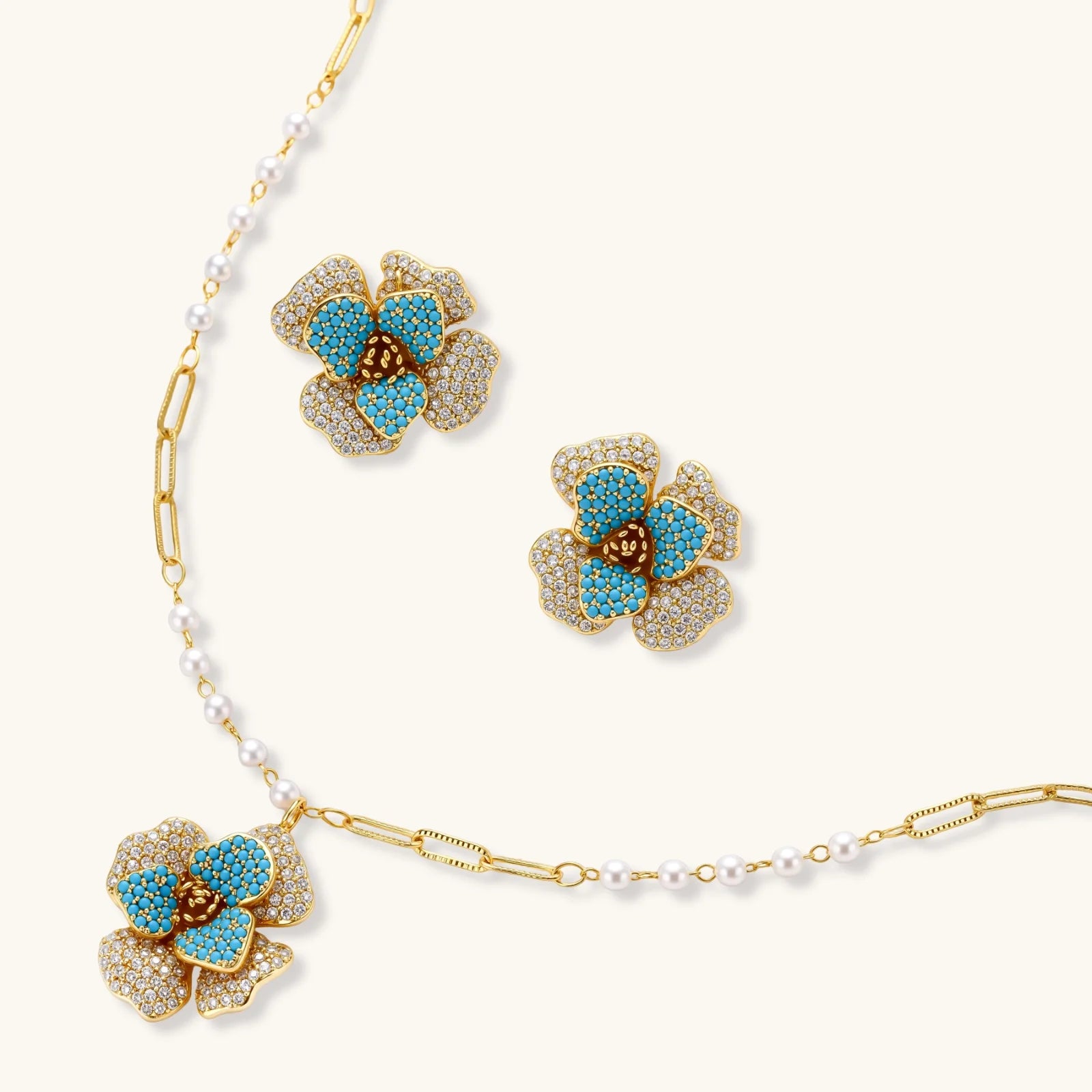 14K gold-plated floral jewelry set with blue cubic zirconia centers and pearl chain details on white background.