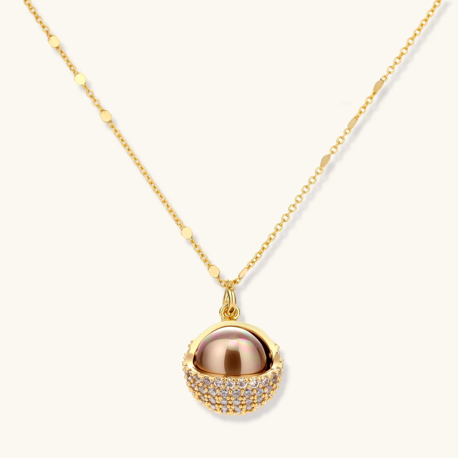 Elegant spherical pendant necklace and earrings set featuring crystal-pavé bottom half in gold or silver finish on white background.