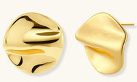 Close-up of organic gold-plated sterling silver stud earrings with flowing sculptural design and curved cut-outs