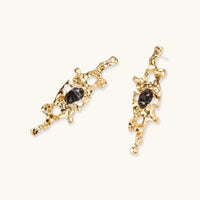 Elongated sculptural earrings with organic openwork design in eco-zinc alloy and dark resin accents on white background.