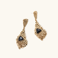Gold-toned geometric mesh earrings with black triangular resin stones and fringe detail on neutral background
