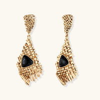 Gold-toned geometric mesh earrings with black triangular resin stones and fringe detail on neutral background